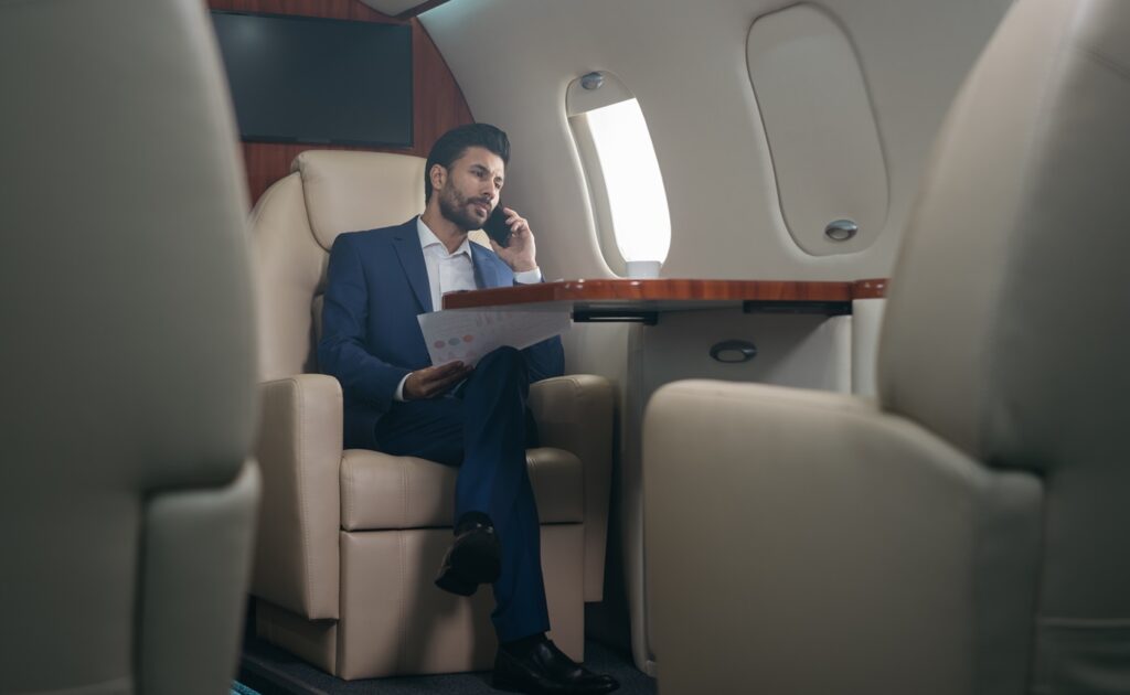 pensive middle eastern businessman talking on mobile phone, holding financial report working with documents sitting in plane