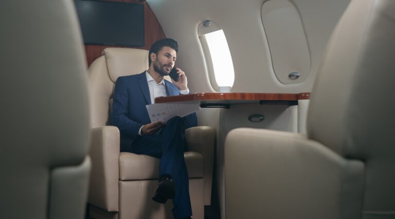 handsome pensive middle eastern businessman talking on mobile phone, holding financial report working with documents sitting in plane