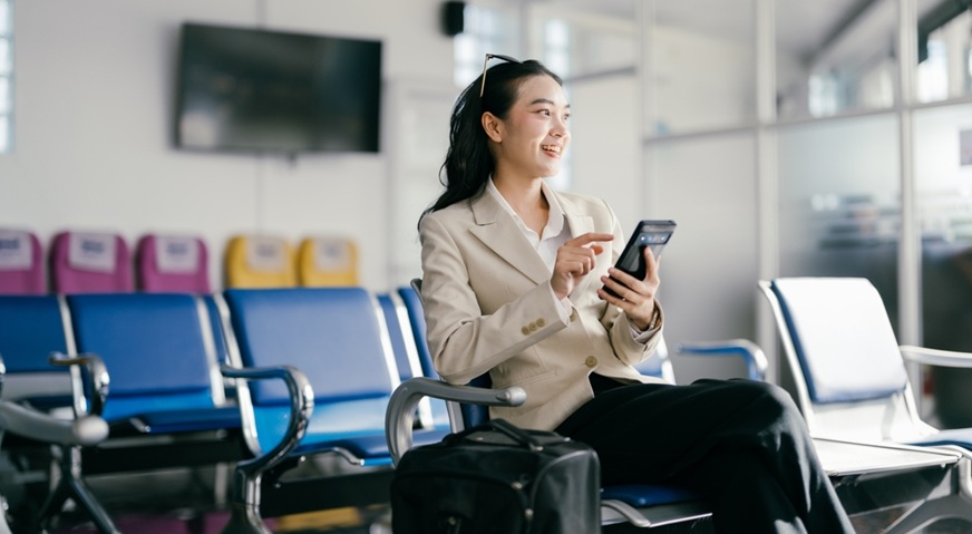 woman in a business suit using her phone while sitting in an airport lounge, ready for travel