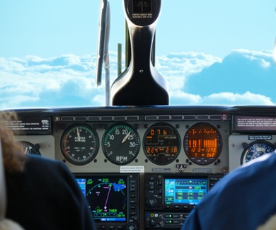 Small twin turbo engine airplane cockpit view while in flight with gauges lit up and fluffy white and blue clouds in the window